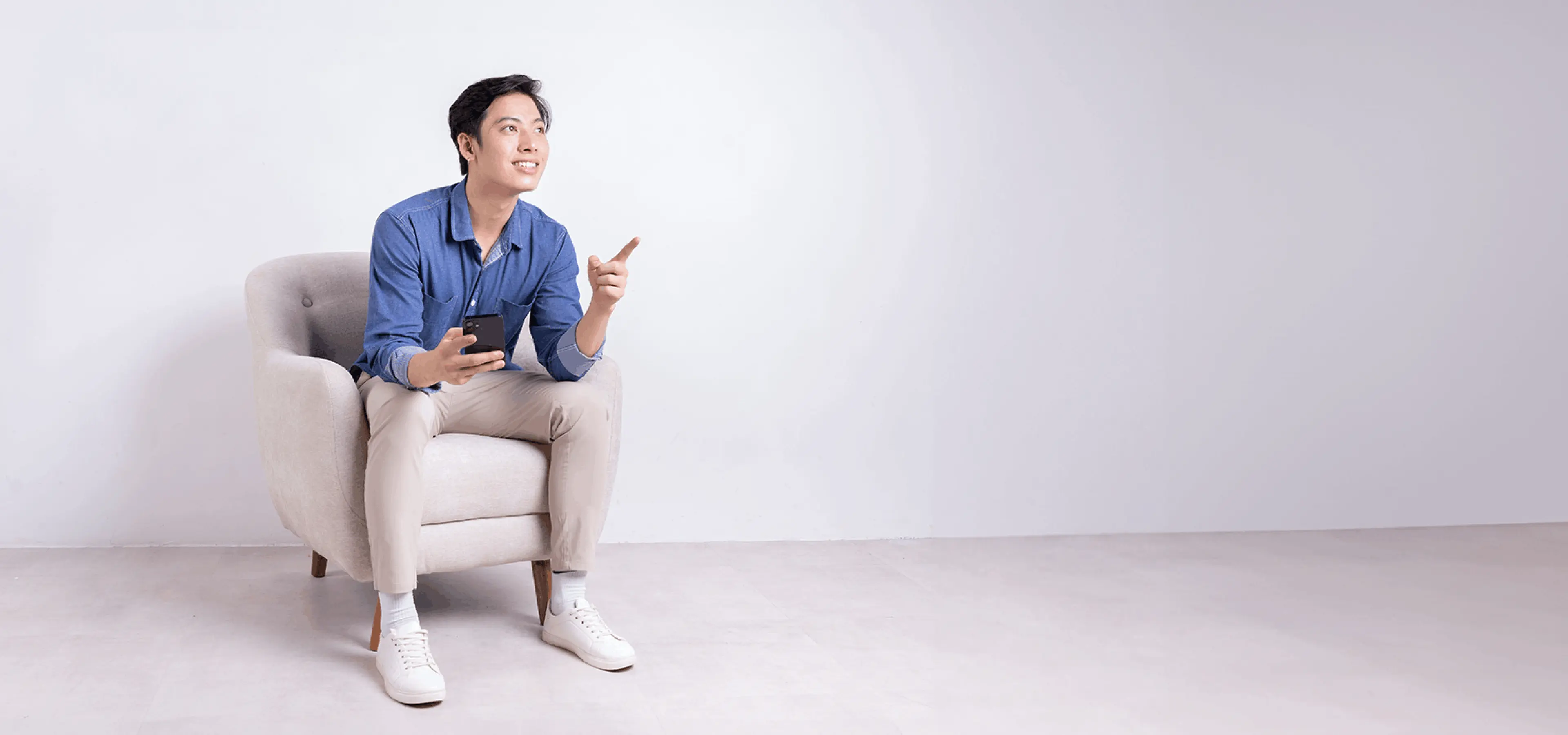 A young man sitting on a couch and holding a cellphone.