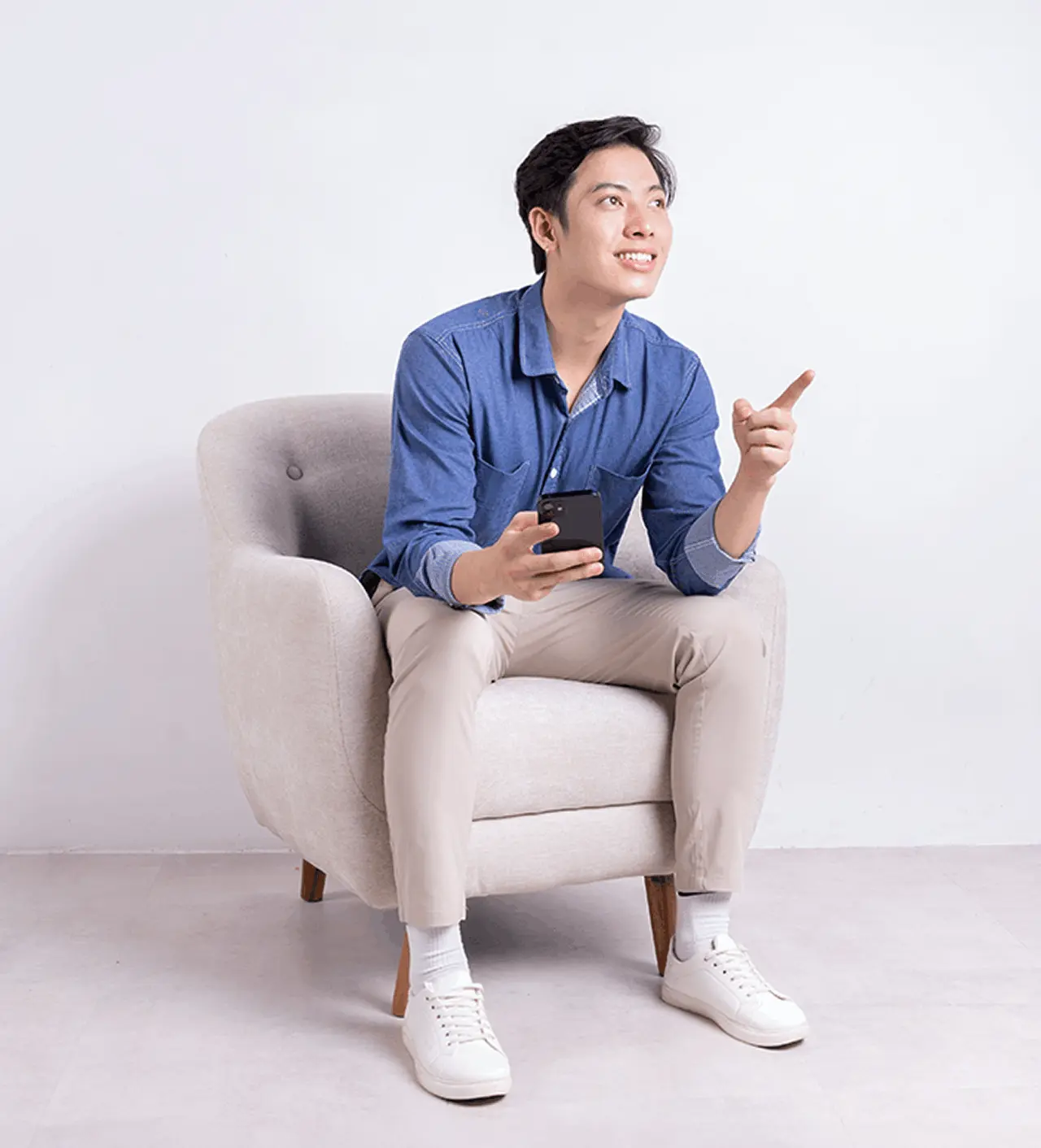 A young man sitting on a couch and holding a cellphone.